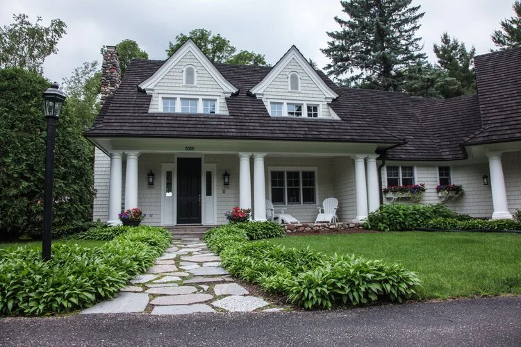 White house with dark shake roof, twin gables, and garden path.