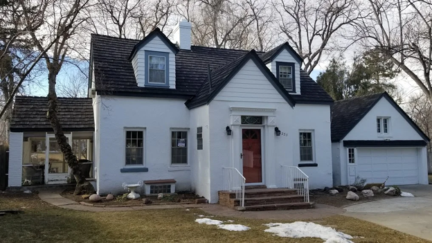 White cottage-style home with a dark CEDUR roof and a red front door.