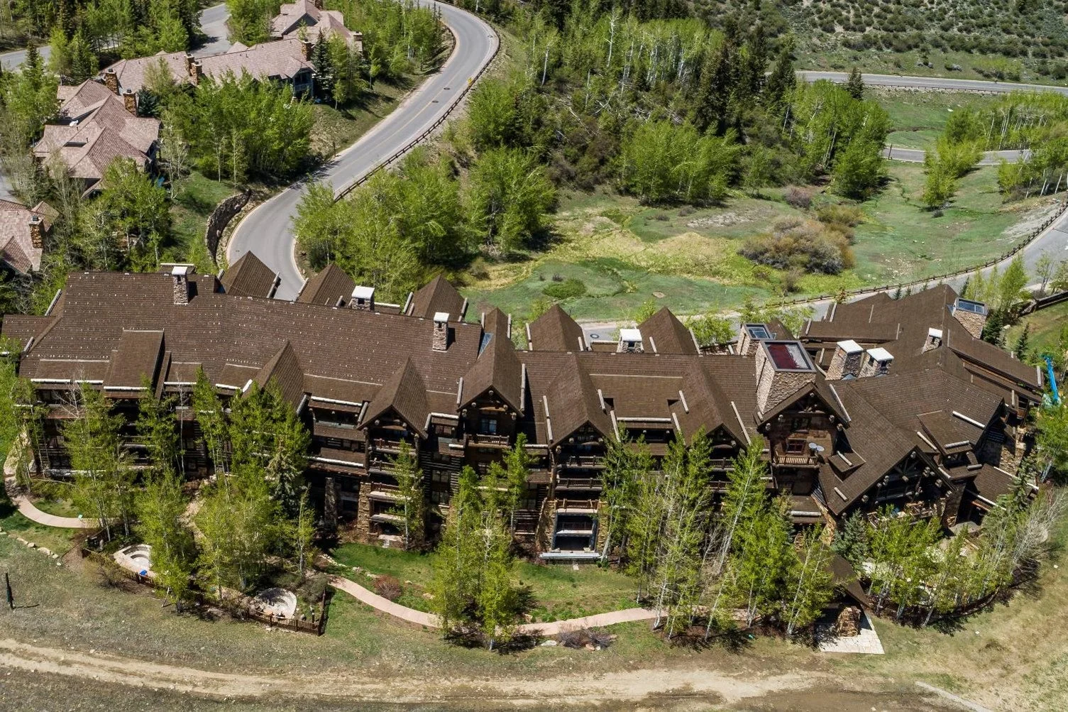 Mountain lodge surrounded by trees with ski slopes and snow patches in the background.