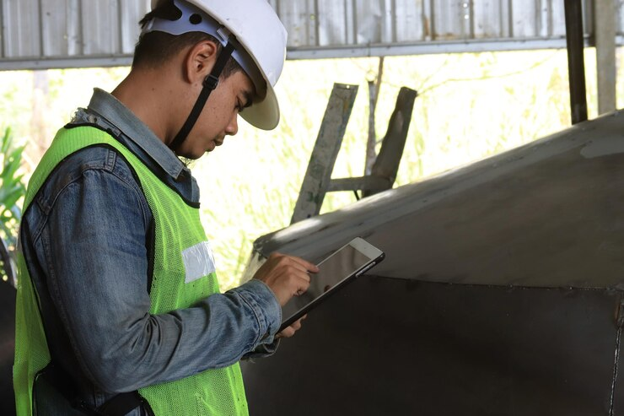 Man in safety gear using a tablet to file a roof claim on-site.