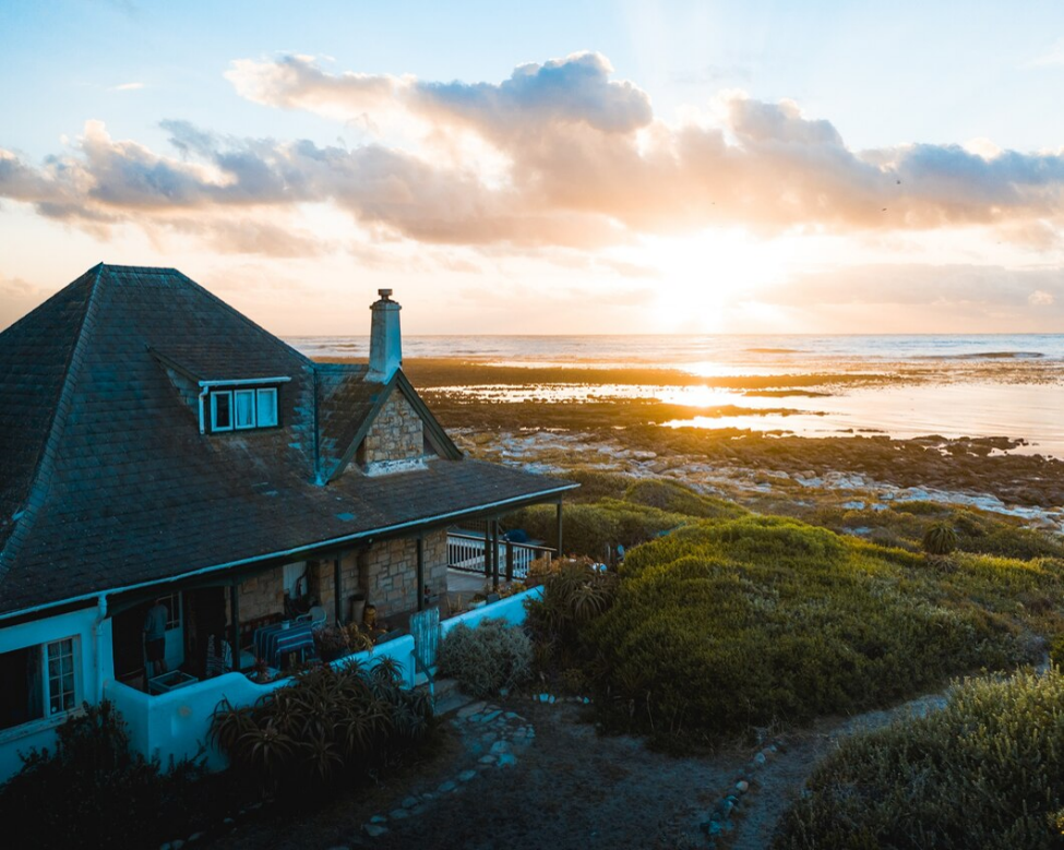 House with a shingle roof by the shoreline, captured at sunset with water views.