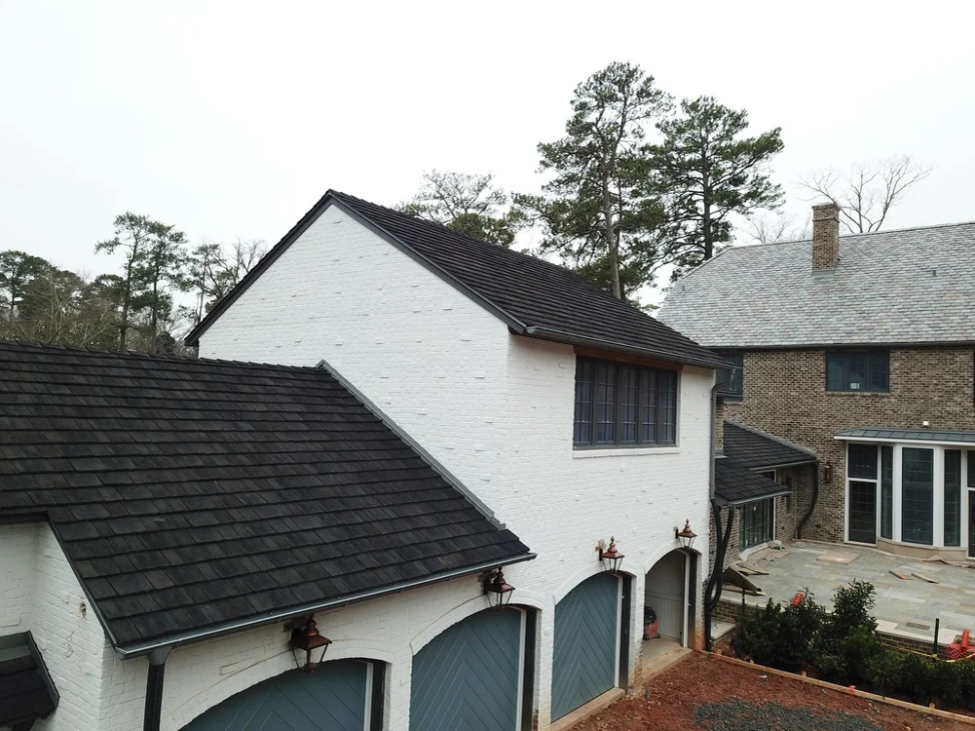 Synthetic cedar shake roof installed on a white brick home with multiple rooflines and attached garage.
