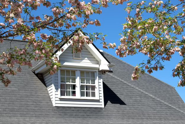 White gable dormer with asphalt shingles framed by blooming branches.