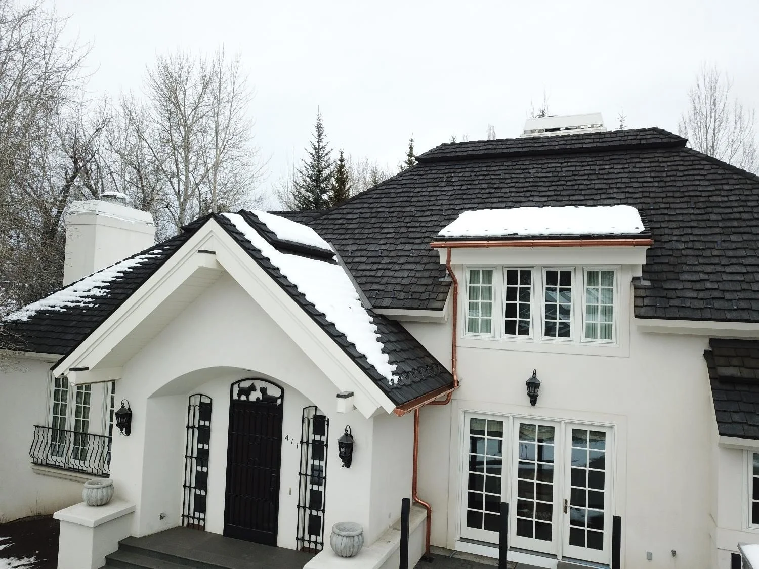 Dark composite shake roof with snow coverage and copper gutters on a residential home.
