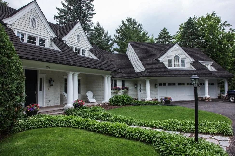 White home with dark synthetic cedar shake roof and landscaped front yard.